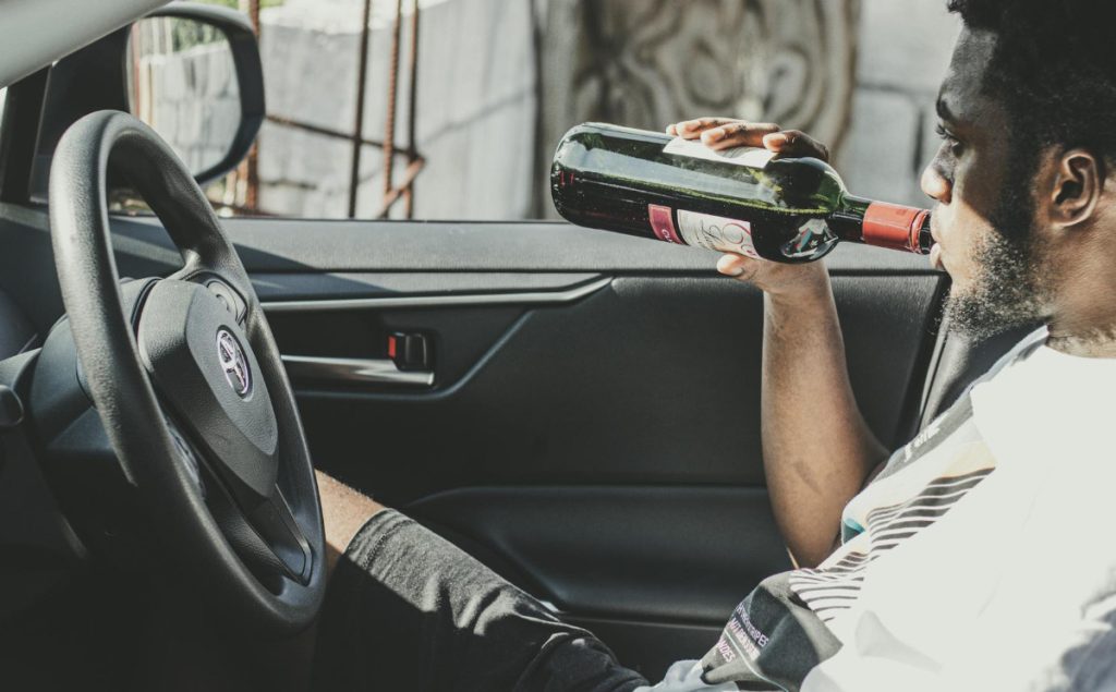 Motorist drinking wine behind the wheel of his vehicle.